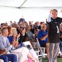 President Tom Haas in front of the crowd at the Jamie Hosford Football Center dedication, pointing to the back of the jersey with his thumbs.